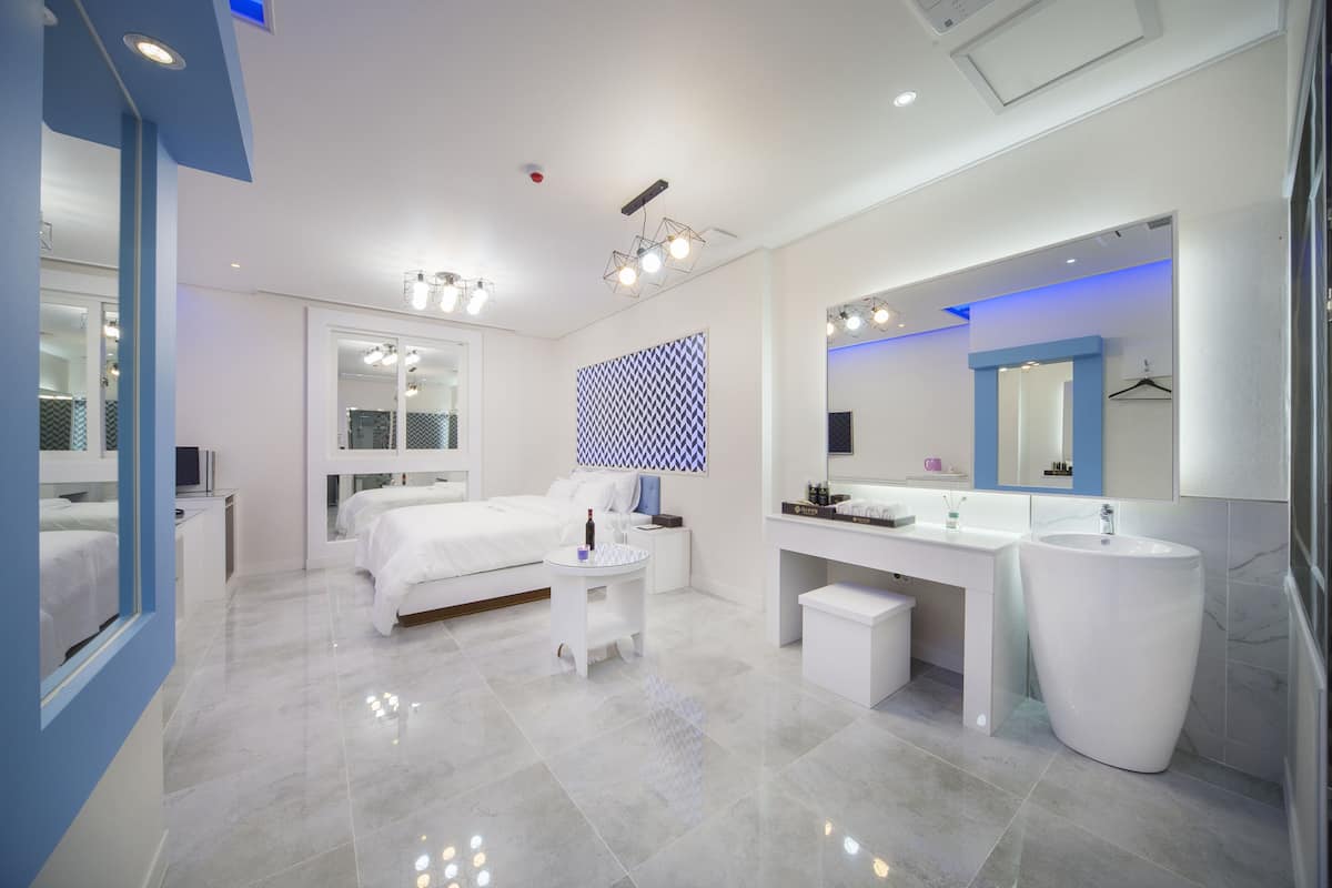 A modern hotel room with a large bed, a vanity with a mirror, a round table, and a large white sink.
