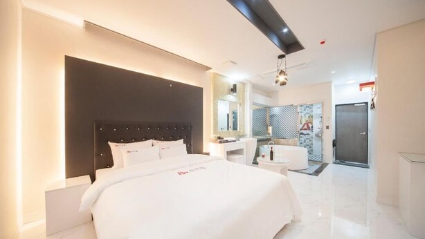 Una habitación de hotel moderna con una cama grande, una mesita de noche, un espejo y un baño visible a través de una puerta abierta.
