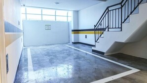 Un pasillo amplio y bien iluminado, con piso de concreto, una escalera con barandillas negras y una puerta con un letrero.