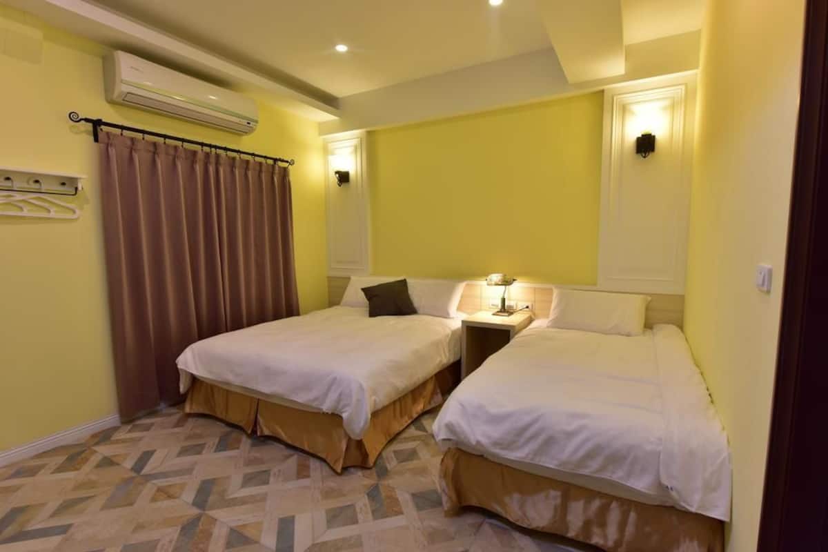 Ein Hotelzimmer mit zwei Betten, einer Wand-Klimaanlage, einem Nachttisch mit Lampe und einem gemusterten Boden.