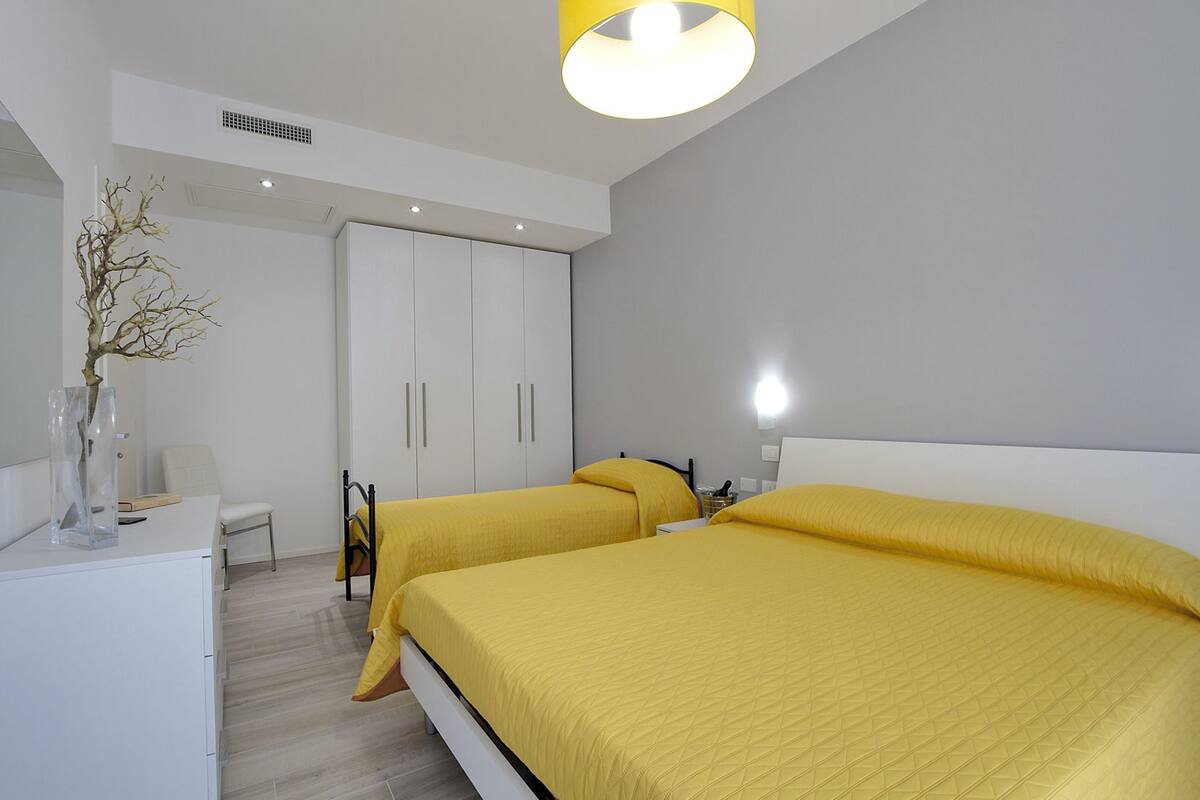 A modern bedroom with two beds, a wardrobe, a desk, and a chair.