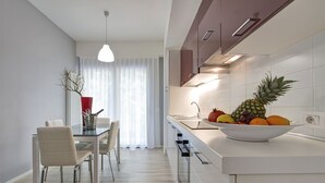 A modern kitchen with white cabinets, a stainless steel sink, and a fruit bowl on the counter. - Residence Armony Misano (Misano Adriatico)