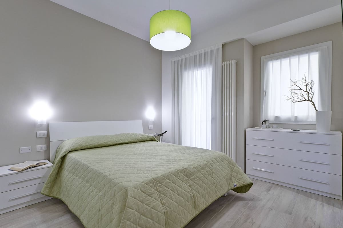 A modern bedroom with a bed, bedside lamps, a dresser, and a window with curtains.