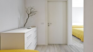 A bedroom with a white dresser, a door, and a bed with a yellow bedspread.
