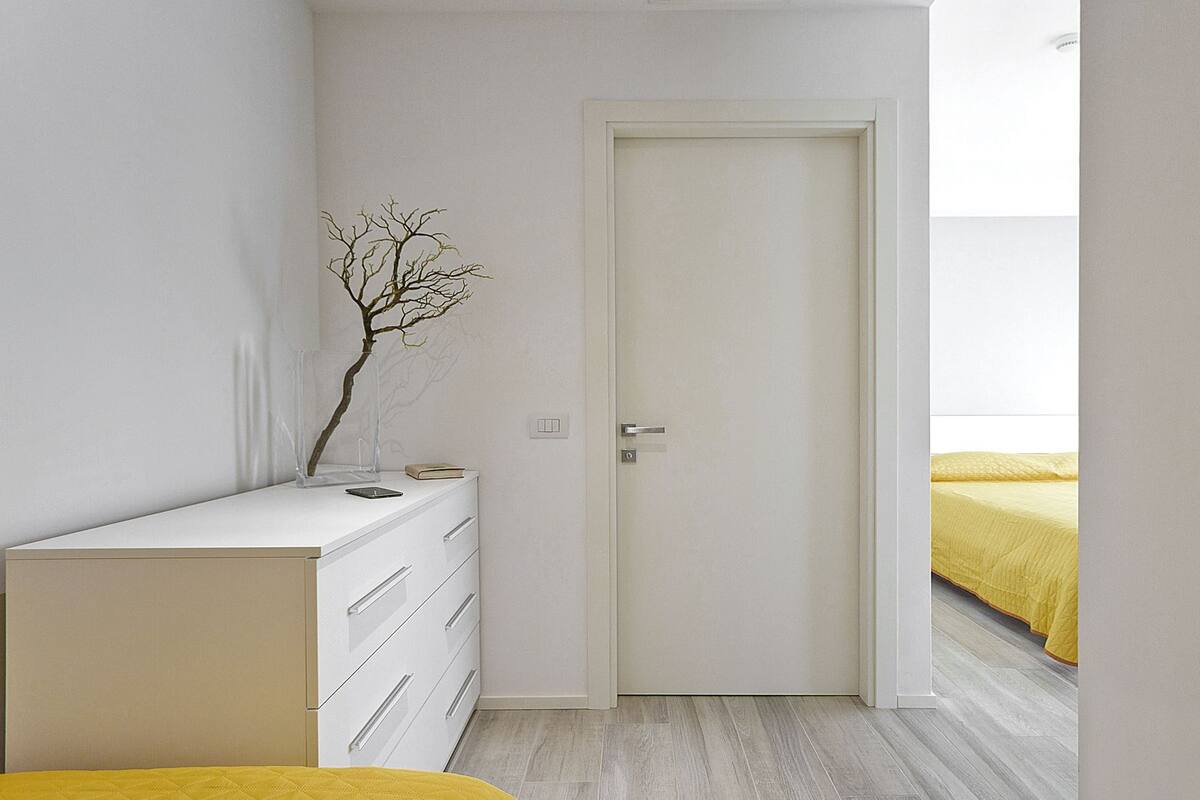 A bedroom with a white dresser, a door, and a bed with a yellow bedspread.