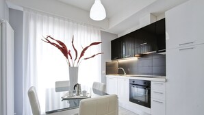 A modern kitchen with white cabinetry, a built-in oven, and a dining area with a glass table and white chairs. - Residence Armony Misano (Misano Adriatico)
