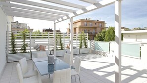 A rooftop terrace with a glass table and white chairs, surrounded by a white pergola. - Residence Armony Misano (Misano Adriatico)