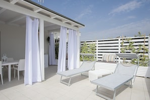 An outdoor patio area with a covered seating area, a dining table, and lounge chairs. - Residence Armony Misano (Misano Adriatico)