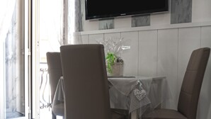 A dining area with a table and four chairs, a potted plant, and a flat-screen TV mounted on the wall. - Voglia di Napoli (Naples)