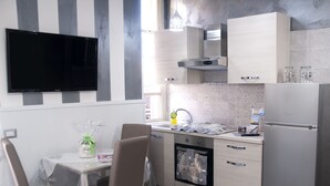 A modern kitchen with a flat-screen TV, stainless steel appliances, and a dining area with chairs and a table. - Voglia di Napoli (Naples)
