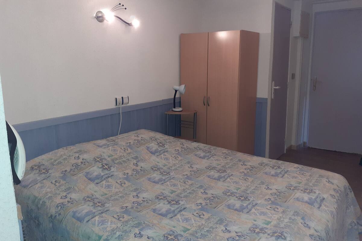 A bedroom with a bed, a wardrobe, a nightstand, and a wall-mounted lamp.