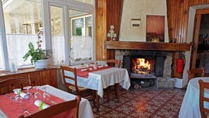 A cozy dining area with a fireplace, wooden walls, and patterned floor tiles. - Hôtel du parc (Val-d'Aigoual)