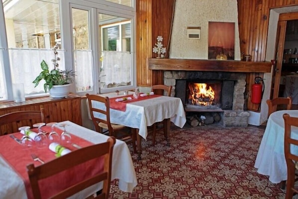 A cozy dining area with a fireplace, wooden walls, and patterned floor tiles. - Hôtel du parc (Val-d'Aigoual)