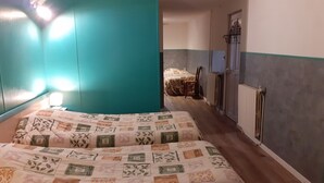 A bedroom with two beds, teal walls, a radiator, and a door leading to another room. - Hôtel du parc (Val-d'Aigoual)