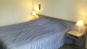 Una cama individual con cubrecama azul, dos lámparas de noche y un teléfono junto a la cama.