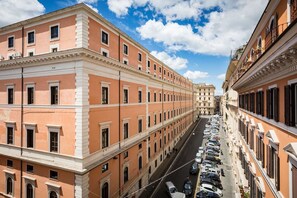 Uma fileira de edifícios históricos com arquitetura uniforme, céu claro e carros estacionados na rua.