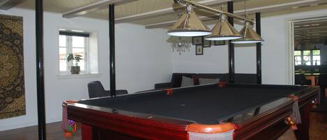 Una mesa de billar en una sala con suelo de madera, una araña y un ventanal con vistas.