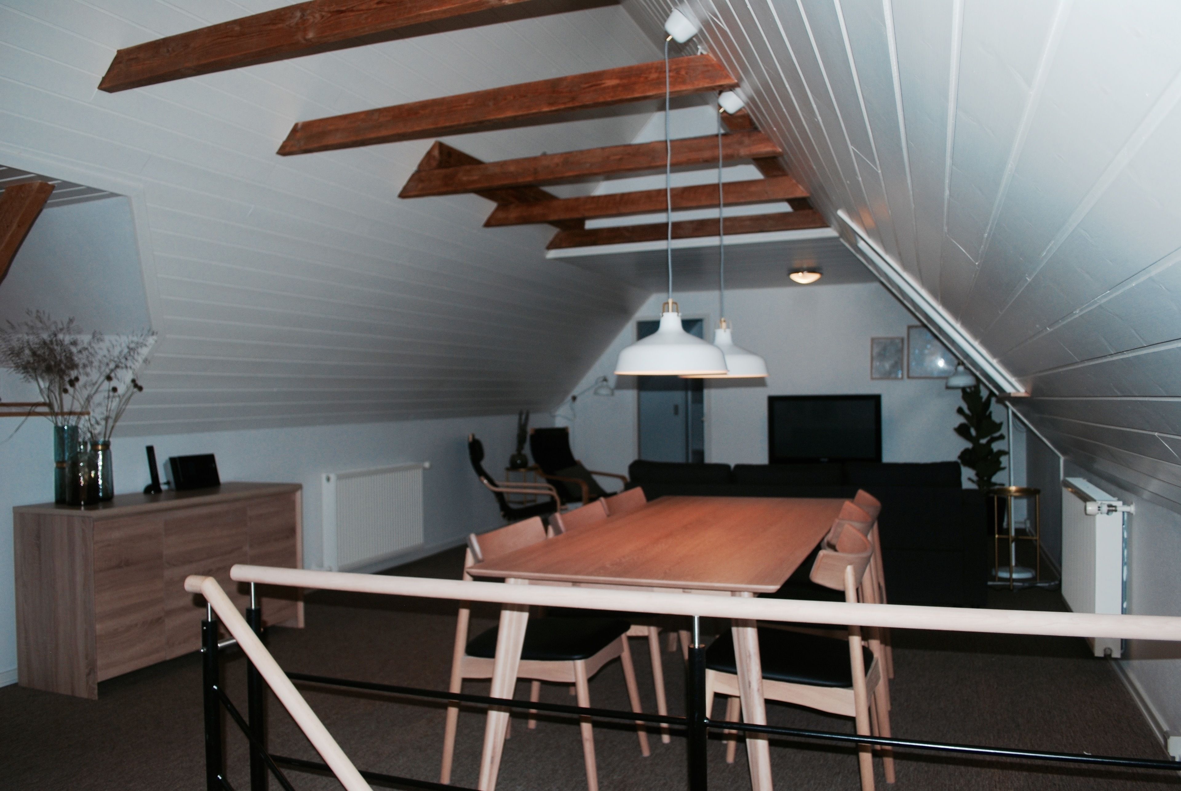 Un coin repas avec une table et des chaises en bois, un luminaire suspendu blanc et une vue sur un escalier.