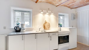 A modern kitchen with white cabinets, a built-in oven, a sink, and a window with a plant on the counter. - Adventure Park Apartments (Ringkobing)