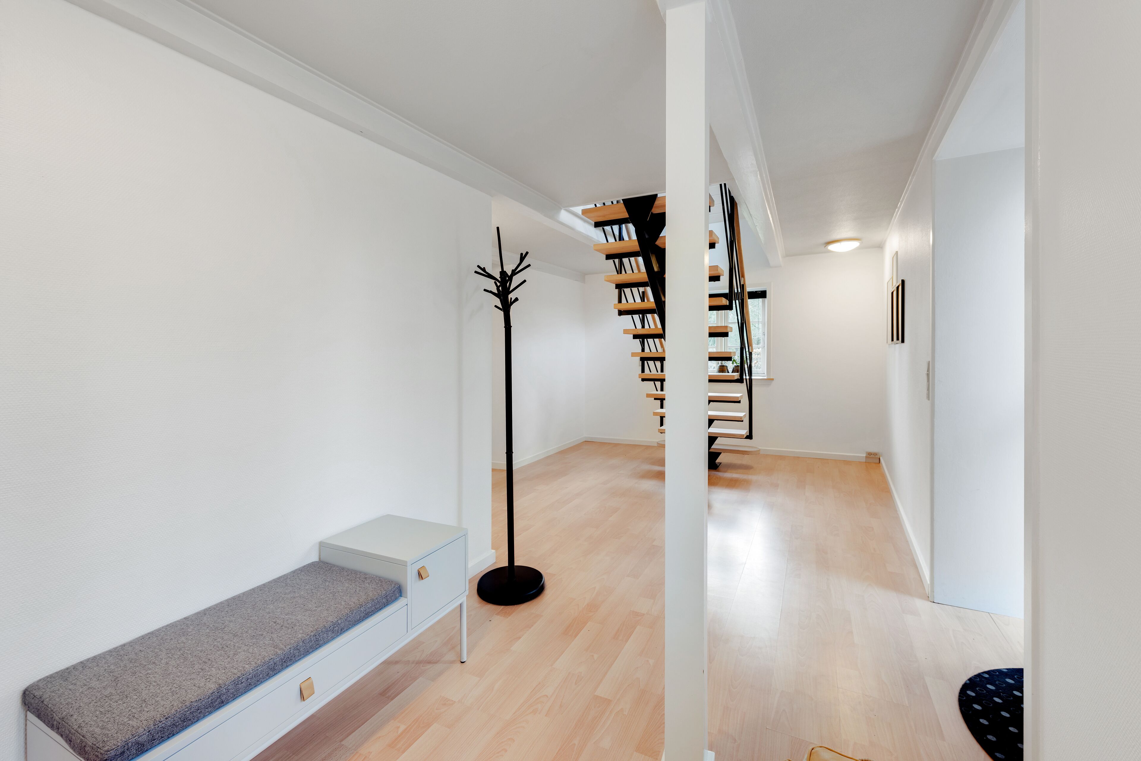 Un pasillo moderno con piso de madera, un banco, una lámpara de pie alta y una escalera con estanterías.