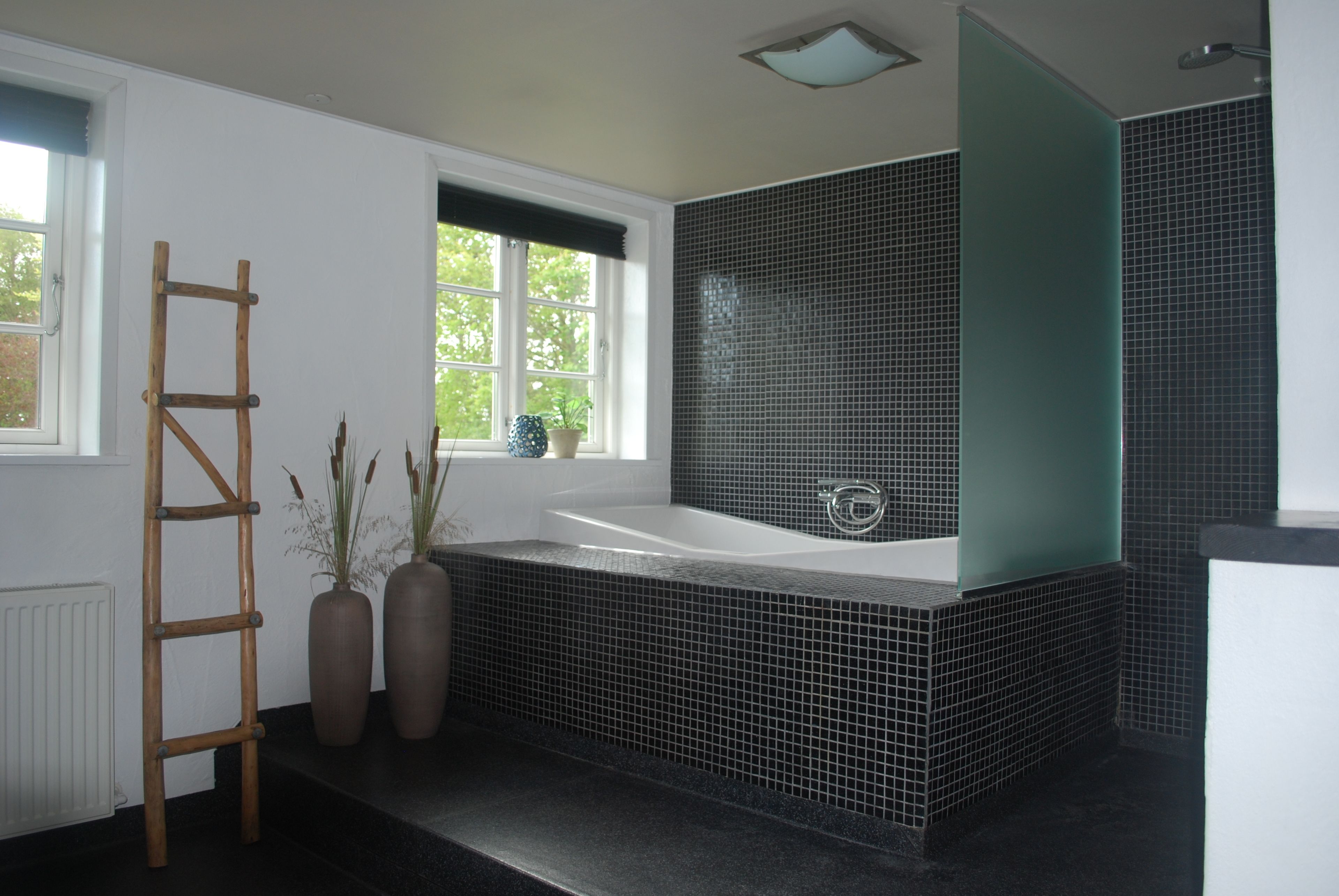 Un baño con una bañera grande, una escalera de madera y dos plantas en macetas.