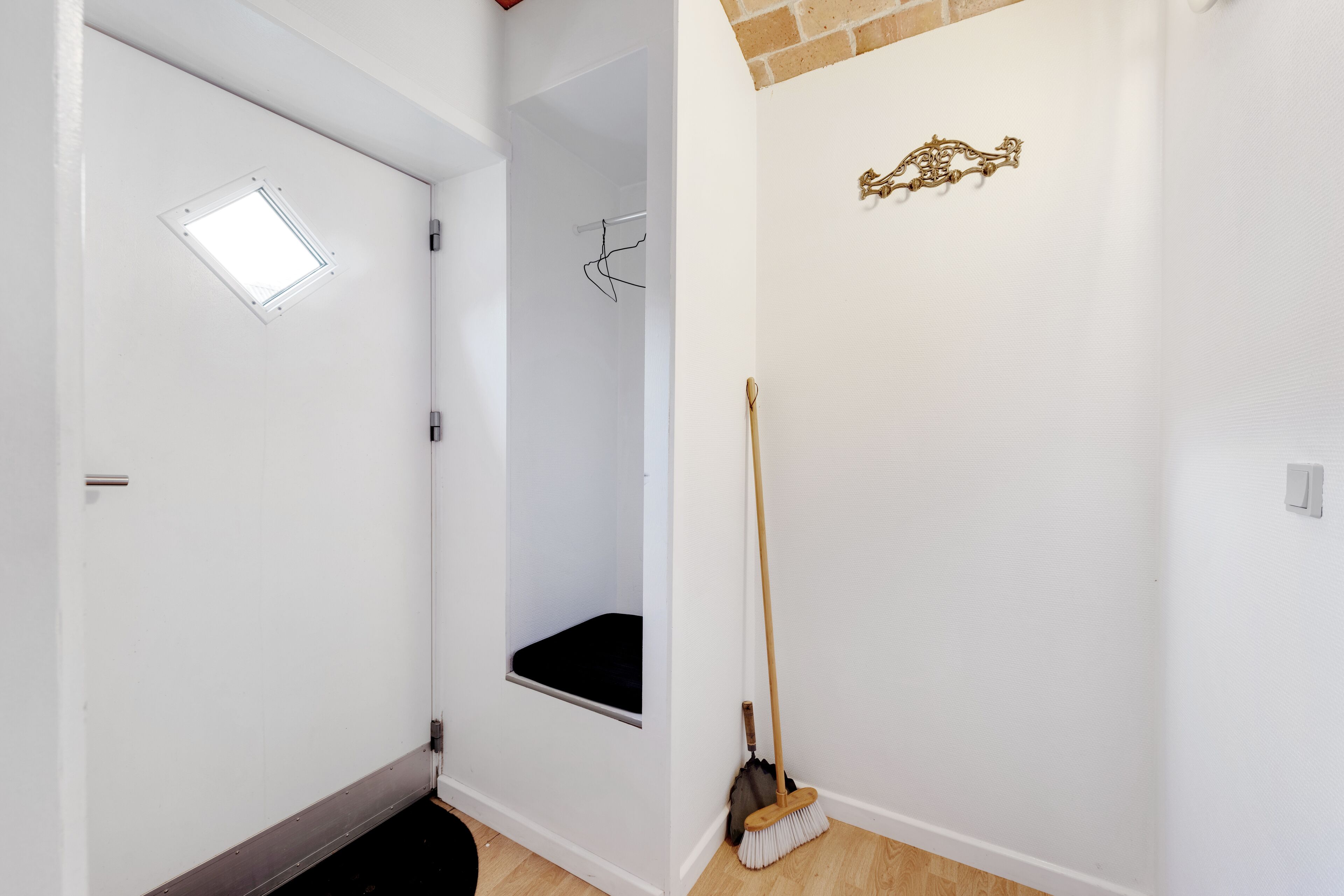 A room with a door, a window, a broom, and a wall-mounted light fixture.