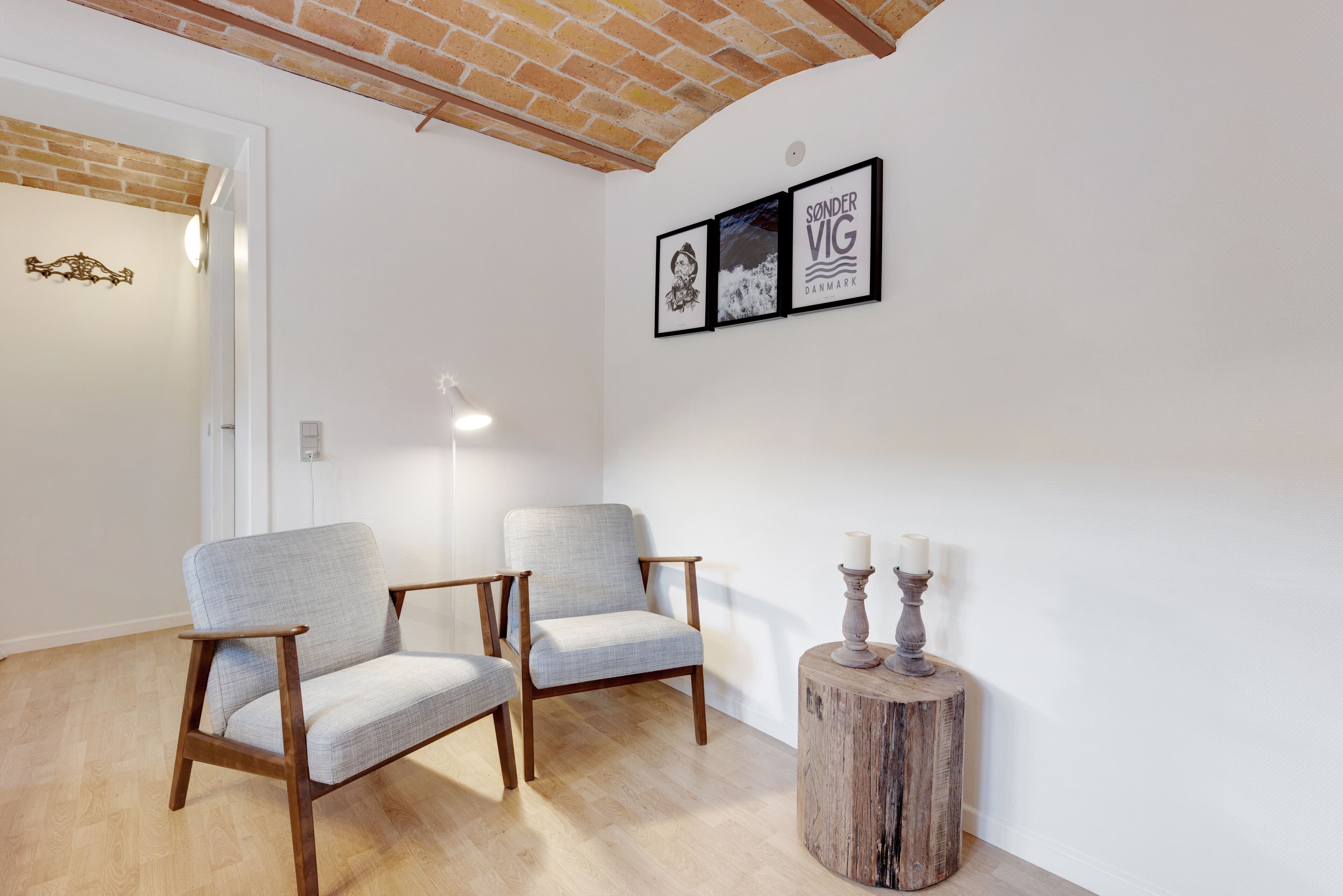 A room with two light grey armchairs, a round wooden side table with candles, and a framed picture of a dog on the wall.