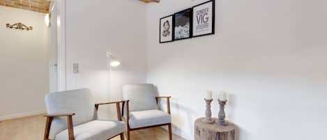 Ein Zimmer mit zwei hellgrauen Sesseln, einem runden Holzhockertisch mit Kerzen und einem gerahmten Bild von einem Hund an der Wand.