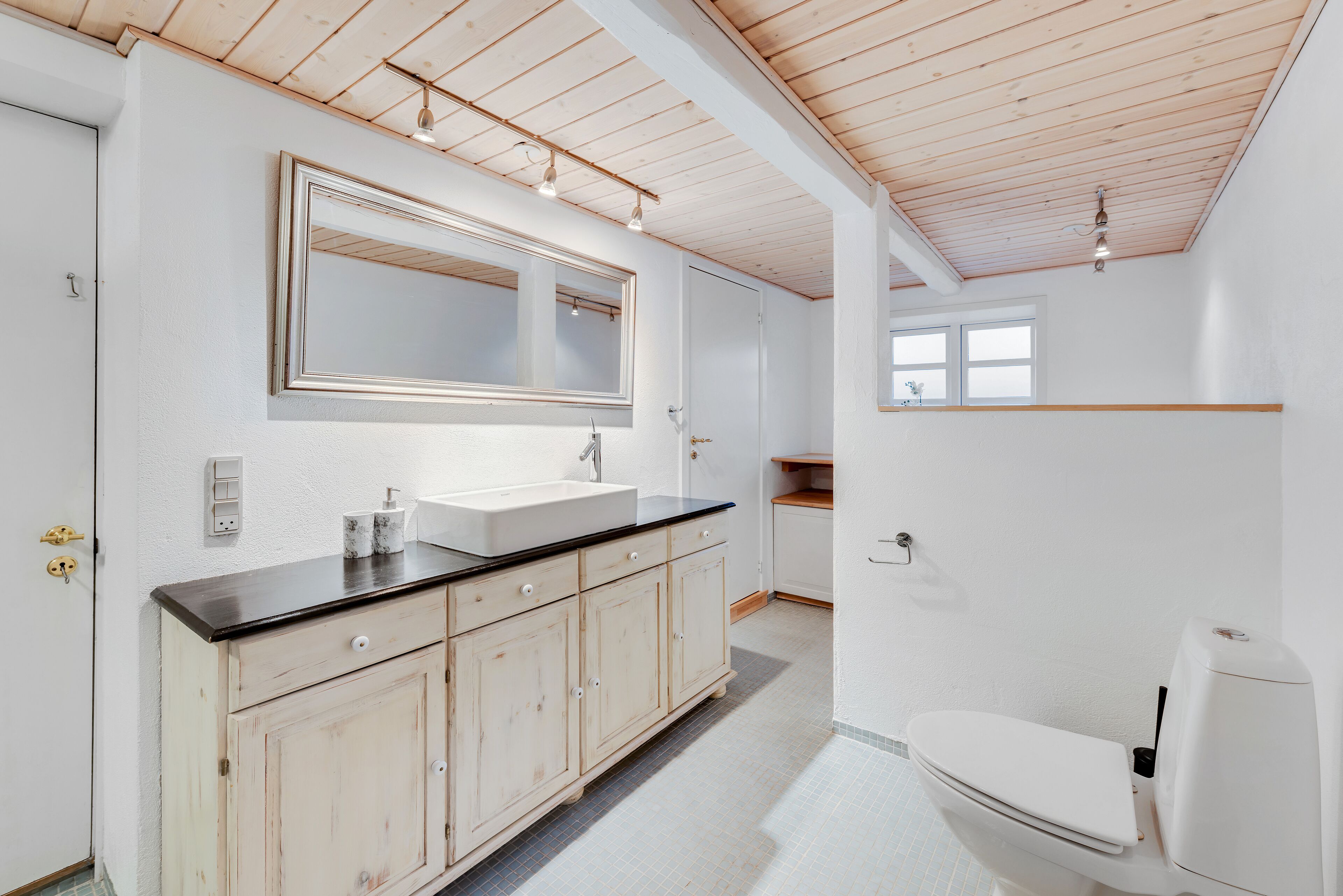 Une salle de bain avec un lavabo blanc, des meubles en bois, un grand miroir et des toilettes blanches.
