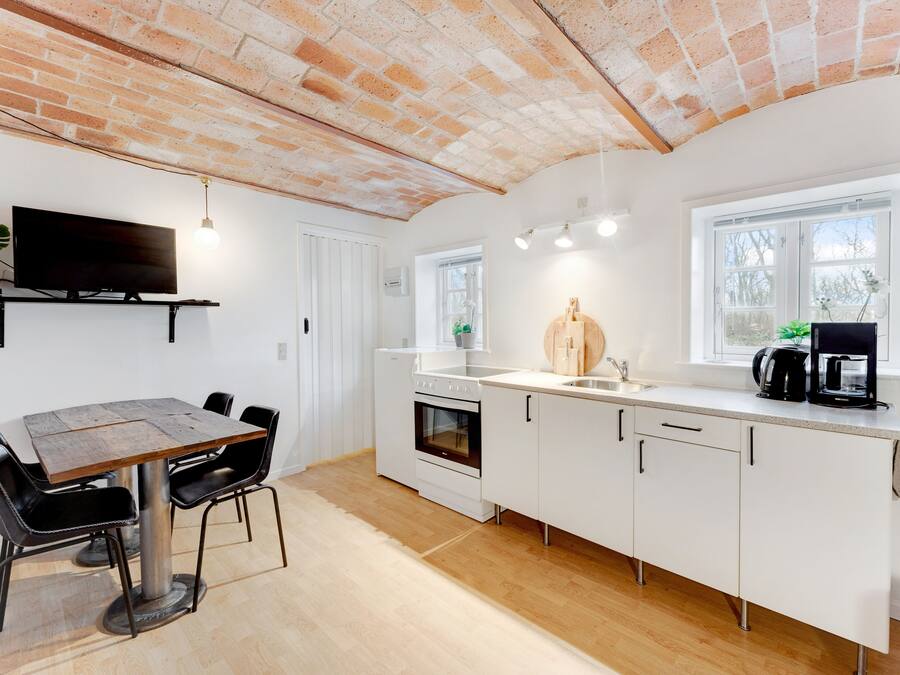 Una cocina moderna con armarios blancos, una mesa de comedor de madera y techo de ladrillo.
