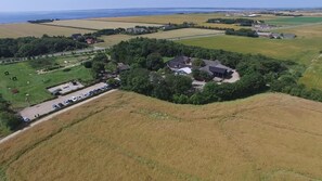 An aerial view of a rural area with a cluster of houses surrounded by fields, a parking lot, and a body of water in the distance. - Adventure Park Apartments (Ringkobing)