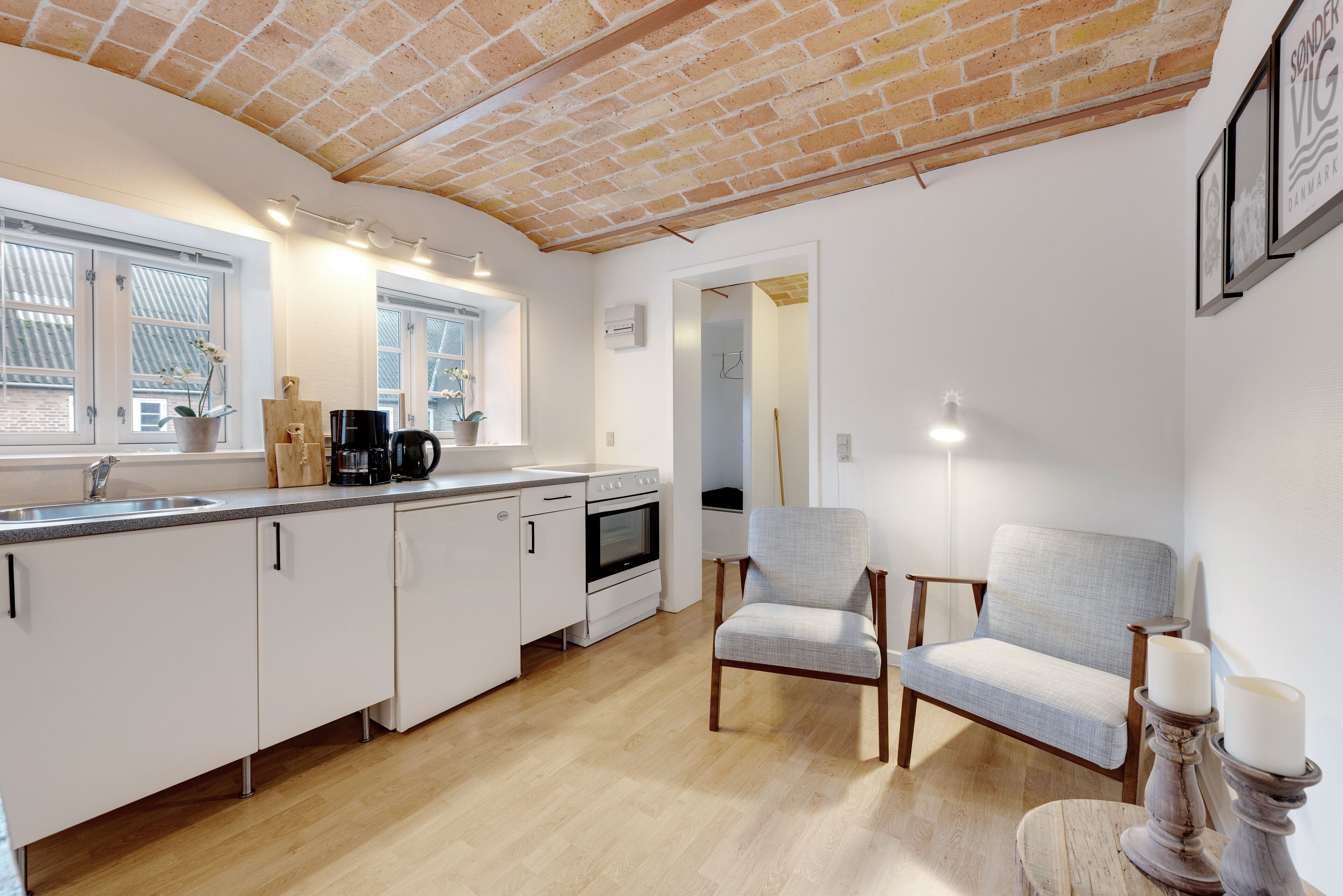A modern kitchen with white cabinets, a brick ceiling, and a dining area with two chairs and a table.