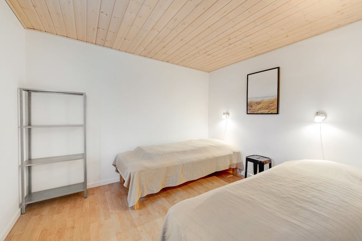 Ein Schlafzimmer mit Holzboden, einem Metallregal, zwei Betten, einem kleinen Tisch und Wandleuchten.