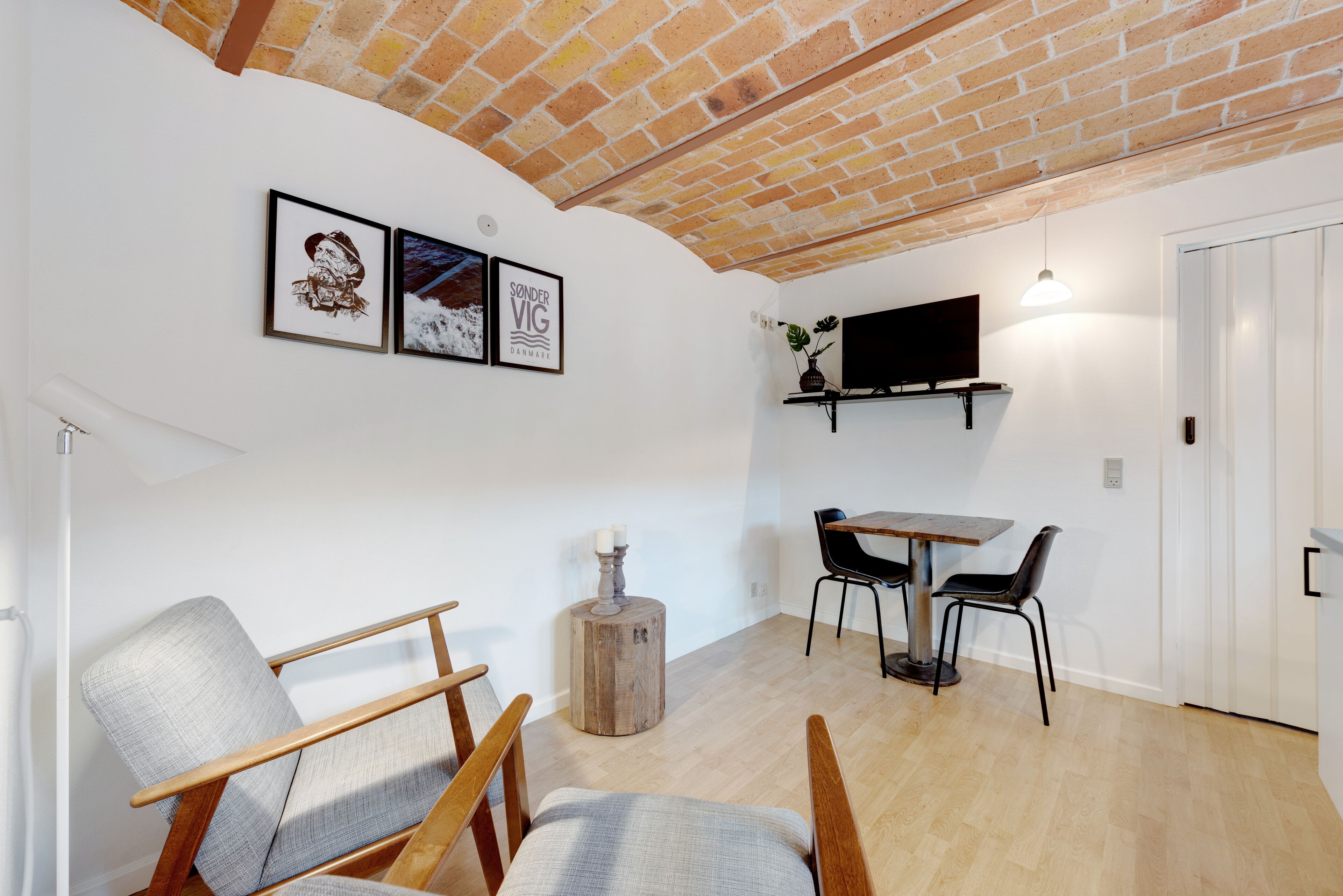 A room with a brick ceiling, a flat-screen TV mounted on a wall, a dining table with chairs, and a small round wooden stool.