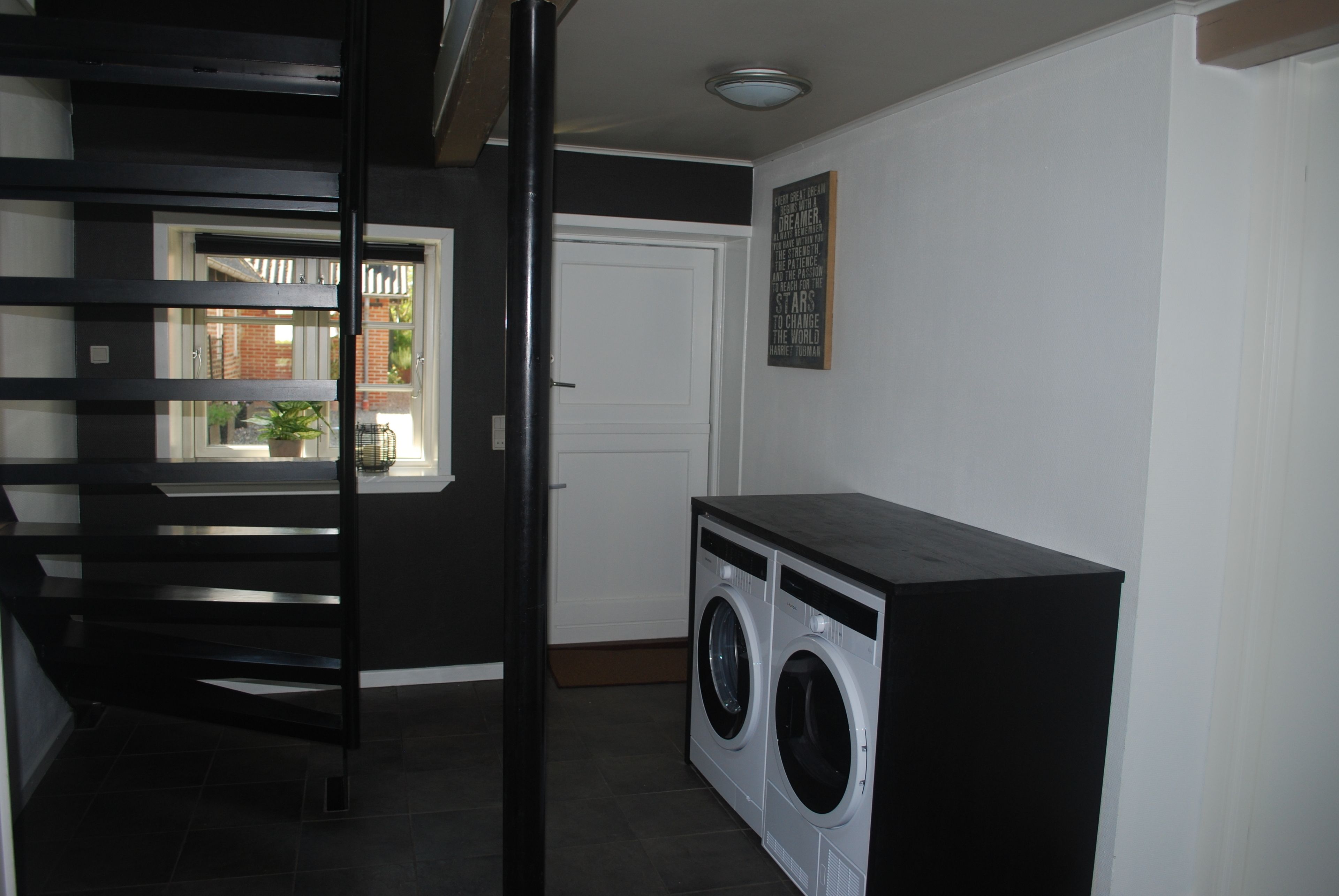 A laundry area with a washing machine and dryer, a white door, and a window with a view of a brick building.