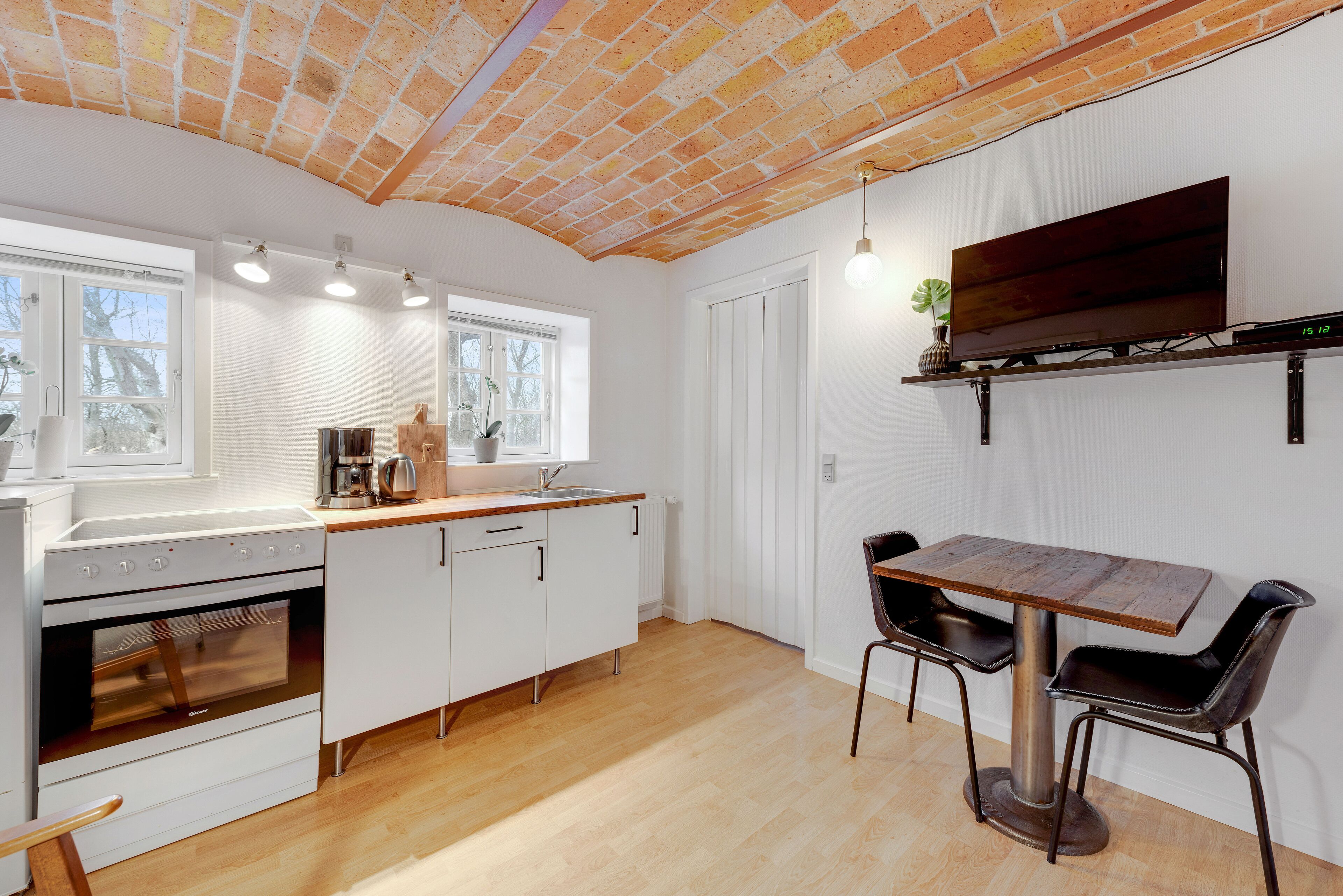 A modern kitchen with white cabinets, a wooden countertop, and a brick ceiling.
