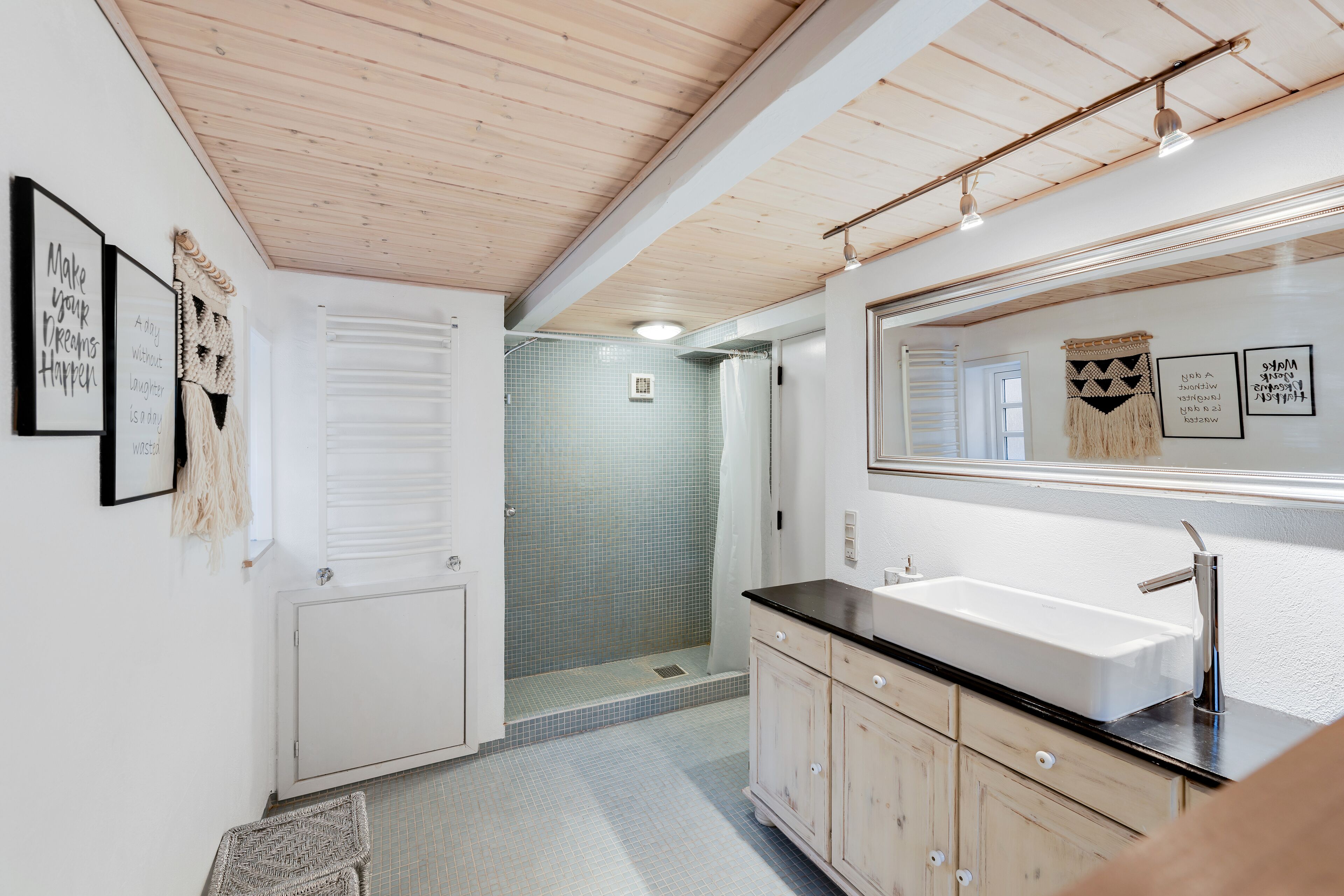 Een moderne badkamer met een grote spiegel, witte tegels, een zwart aanrecht en een douchegedeelte.