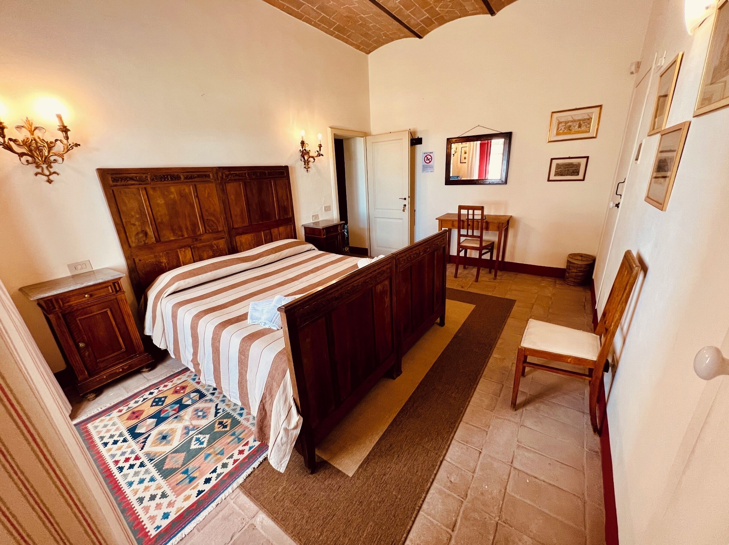 Ein Schlafzimmer mit einem hölzernen Bett, einem kleinen Schreibtisch, einem Stuhl und einem gemusterten Teppich.