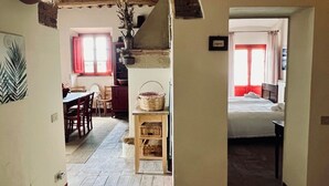 A spacious hallway with a stone floor, leading to a dining area with a table and chairs, and a bedroom with a bed and window. - Fattoria Podere i Luoghi (Casale Marittimo)
