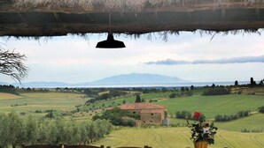 A rustic outdoor dining area with wooden chairs and a table, overlooking a scenic landscape with fields and a distant mountain. - Fattoria Podere i Luoghi (Casale Marittimo)