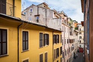 A narrow street with yellow buildings, shuttered windows, and a person walking.