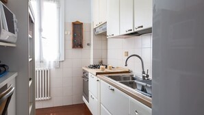 A compact kitchen with white cabinets, a built-in oven, a sink, and a window with curtains. - Via Laurina 40 Apartment (Rome)