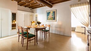 A dining area with wooden chairs and a table, a painting on the wall, and a window with curtains. - Via Laurina 40 Apartment (Rome)