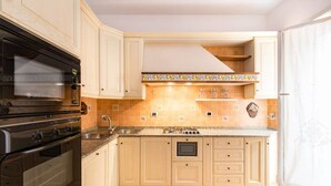 Una cucina con mobili chiari, forno doppio, microonde, lavello e schienale piastrellato.