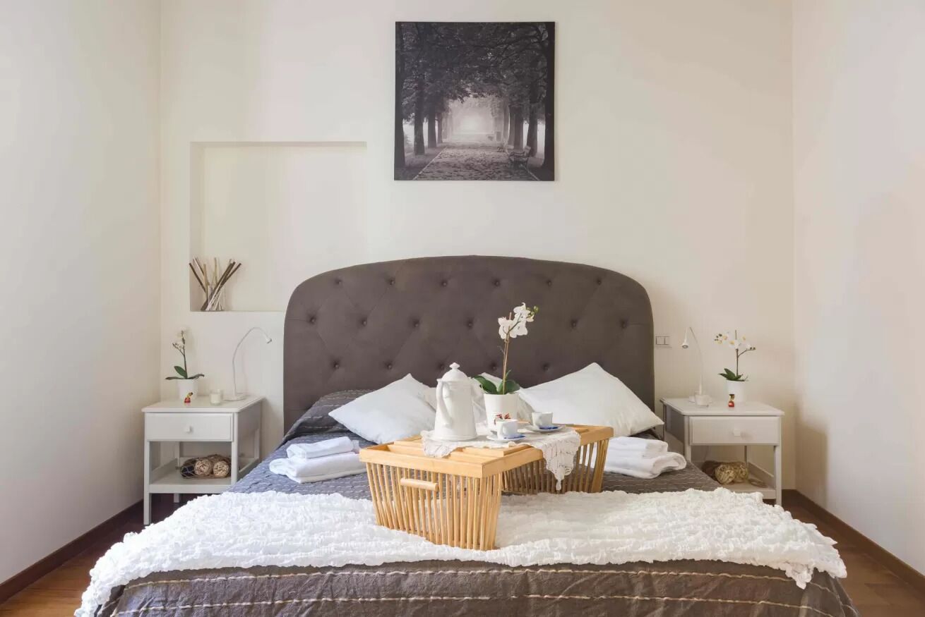 A neatly arranged bedroom with a large bed, two bedside tables, a bedside lamp, and a framed picture on the wall.