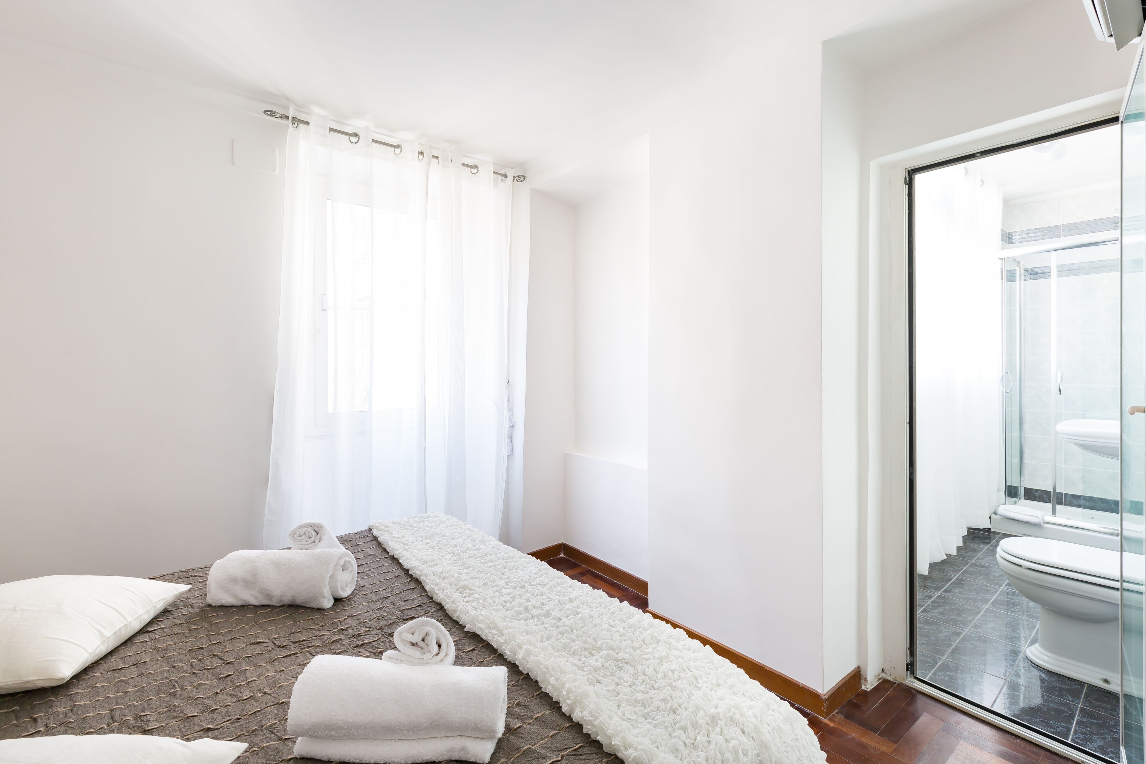 Quarto de hotel moderno com uma cama grande, divisória de chuveiro de vidro e vista para o banheiro.