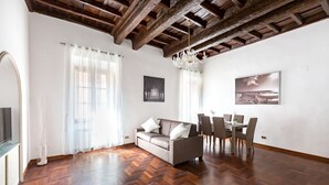 A modern living room with a wooden herringbone floor, a grey sofa with white cushions, a dining table with chairs, and a chandelier. - A World Apart - Trevi Apartments (Rome)