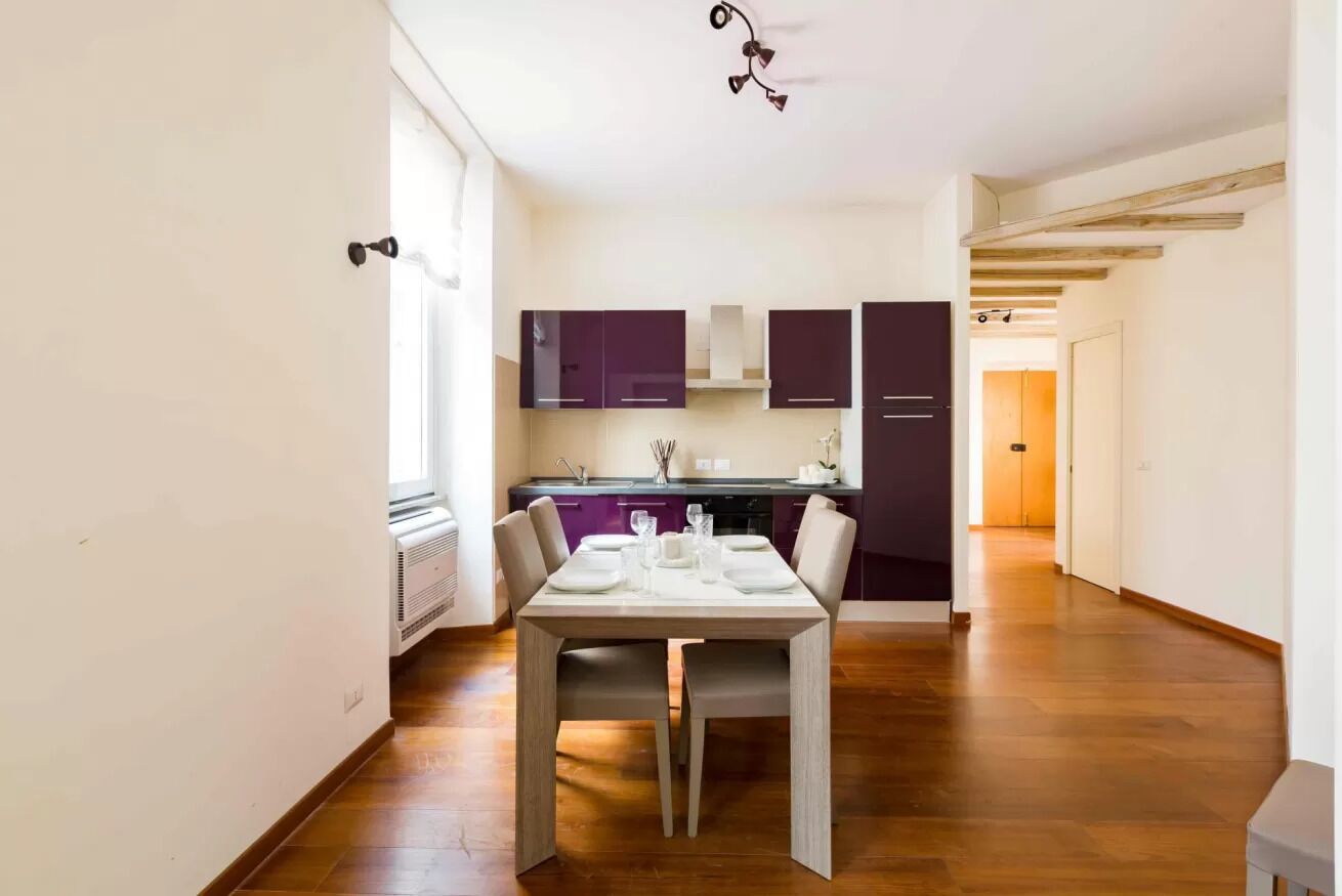 Una cocina moderna con armarios oscuros, una mesa de comedor lista para cuatro personas y suelo de madera.