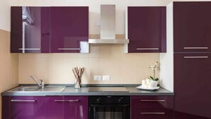 A modern kitchen with purple cabinets, a stainless steel sink, and an oven. - A World Apart - Trevi Apartments (Rome)