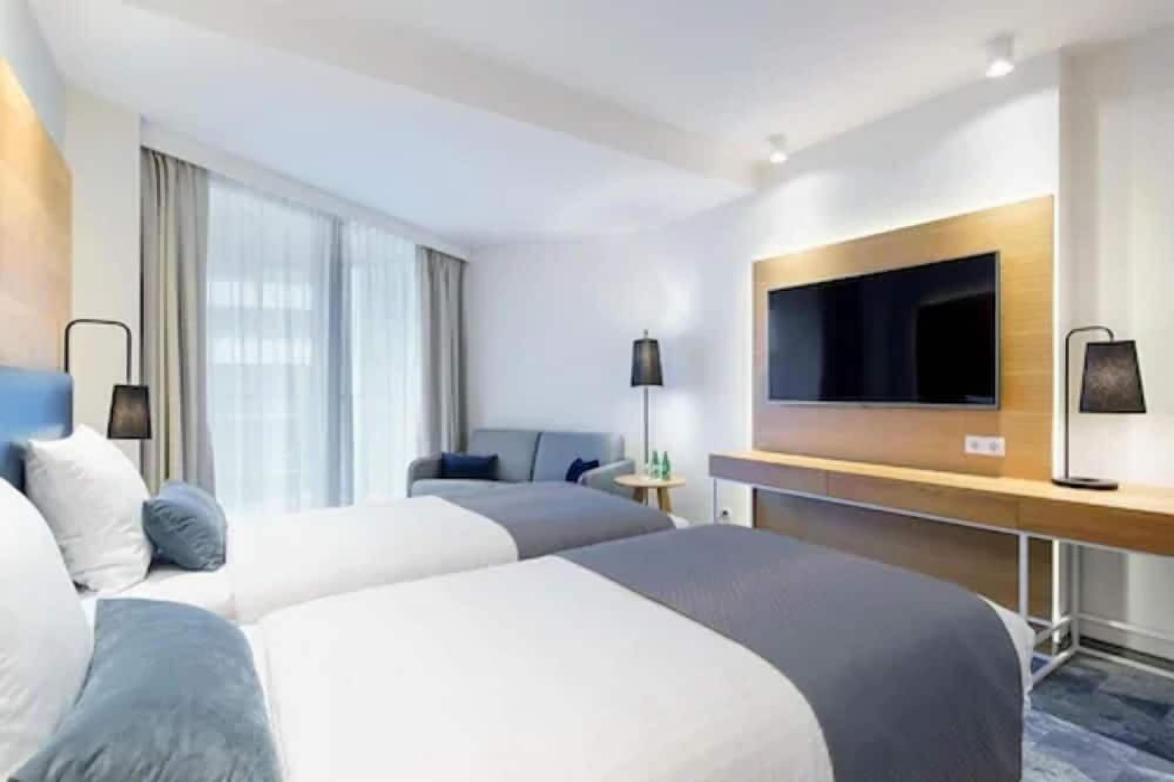 Une chambre d’hôtel avec deux lits, un téléviseur à écran plat fixé au mur, un bureau et une chaise.